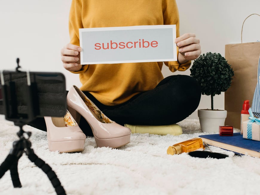 female-fashion-blogger-streaming-home-with-smartphone-subscribe-word